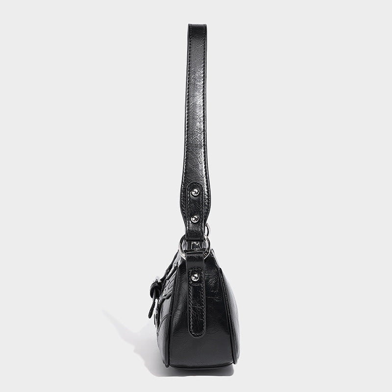 Compact moto-inspired shoulder bag with crisscross grommet strap detail, glossy textured finish, and adjustable crossbody