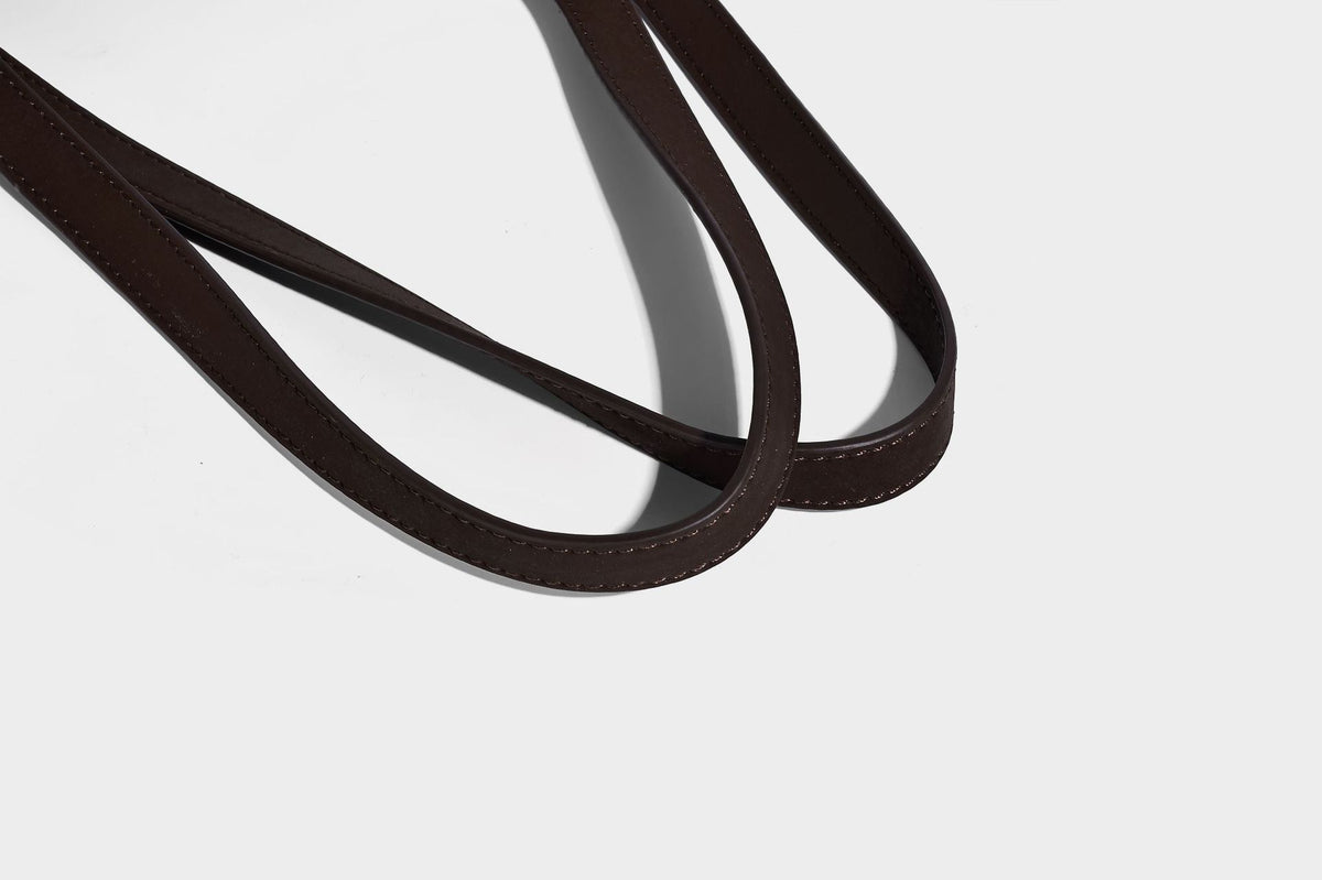 Structured trapezoid shoulder tote in dark brown matte suede-look finish with dual straps, wraparound belt bands