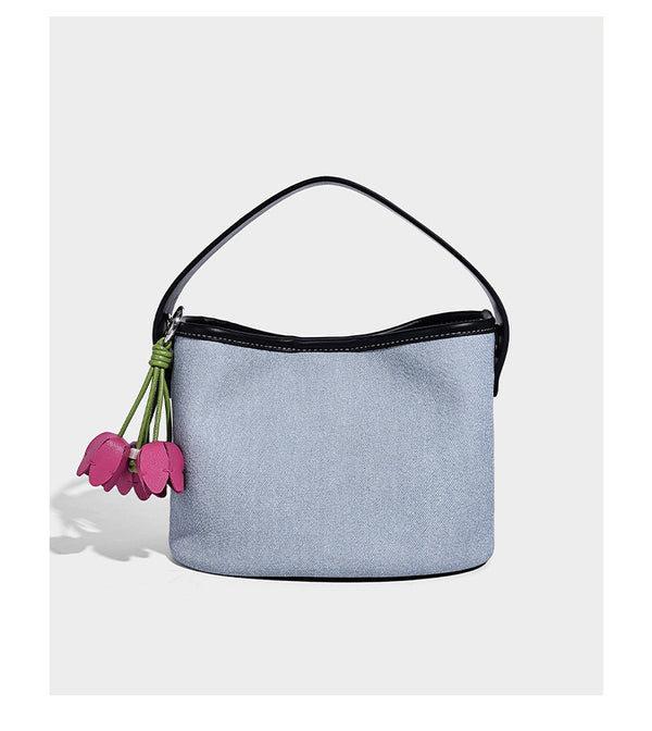 Small denim-look bucket bag with black leather-look trim, pink tulip flower charm, and adjustable crossbody strap, detail