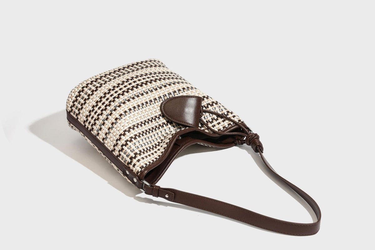 Woven stripe bucket shoulder bag in cream and dark brown with leather-look trim, knotted adjustable strap, and small shield