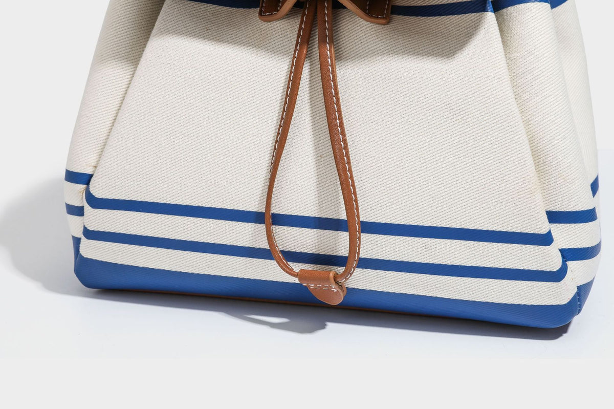 Cream canvas bucket bag with blue horizontal stripes, tan leather-look flap and trim, drawstring closure, silver-tone, detail
