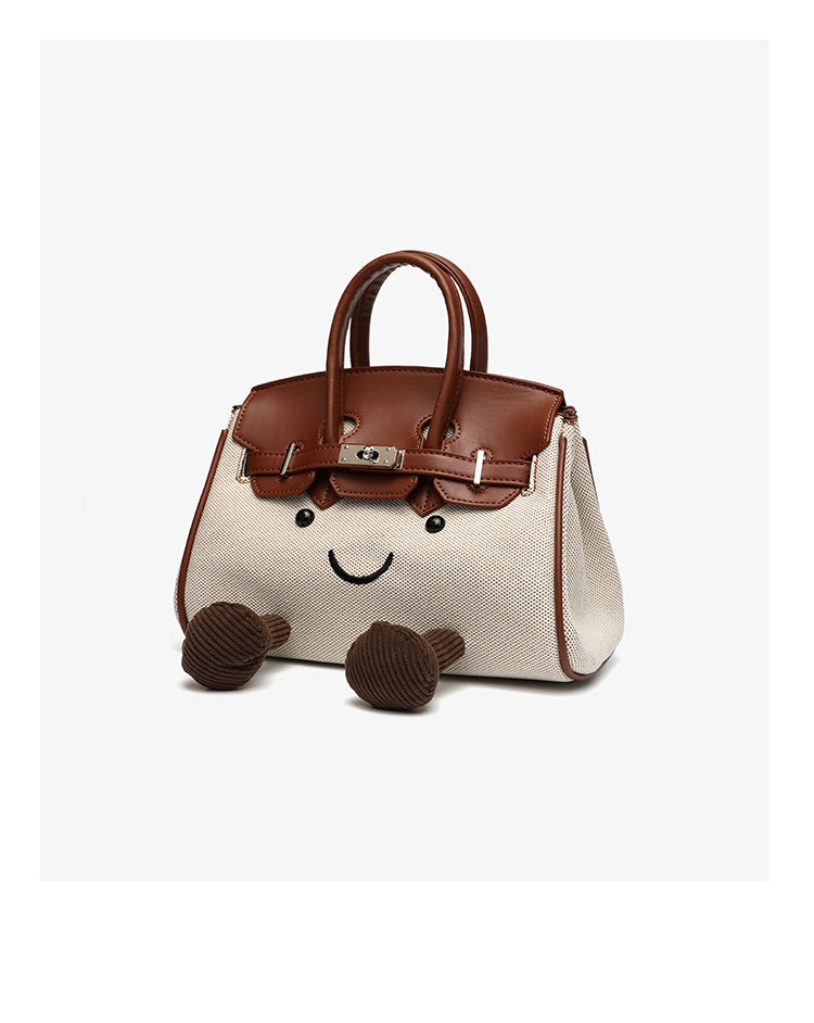 Small structured trapezoid satchel bag with smiling face motif, pom-pom accents, brown leather-look trim, silver-tone, detail