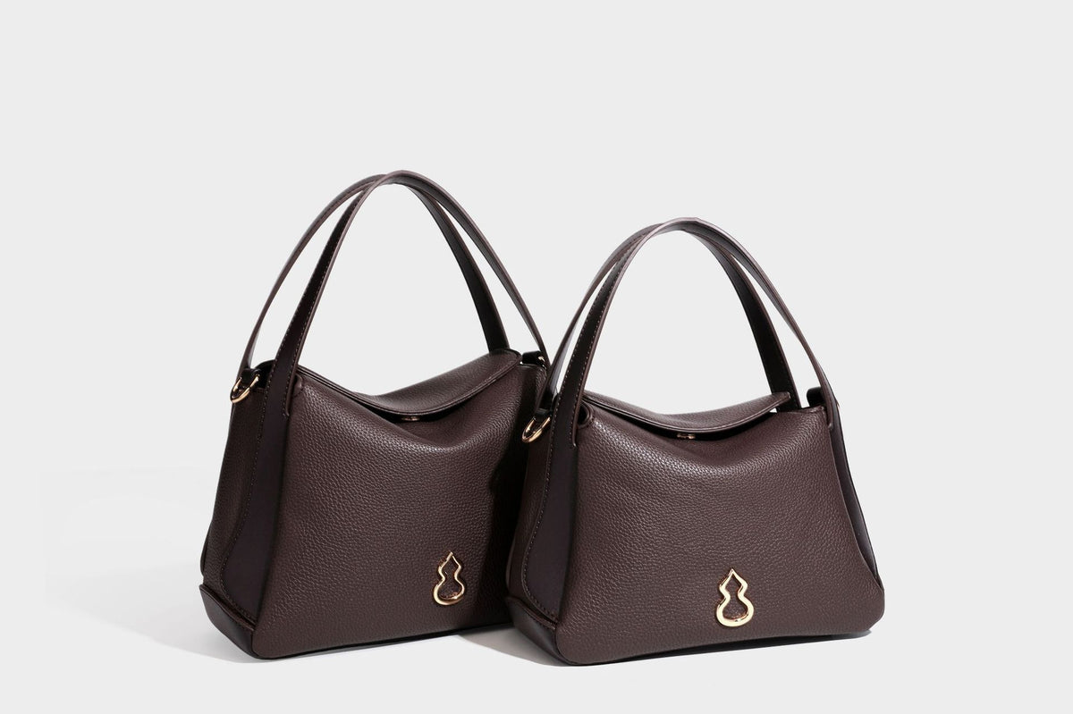 Structured pebbled leather-look shoulder bag with flap top, gold-tone emblem hardware, dual top handles, and detachable