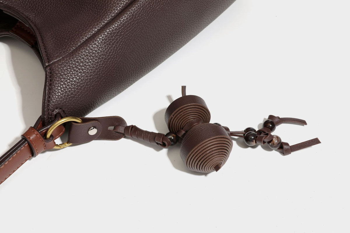 Hobo-Schultertasche in dunklem Espresso mit genarbter Oberfläche, warmen cognacfarbenen Details, verstellbarem schmalem Riemen, goldfarbenen Ringbeschlägen und geknotetem