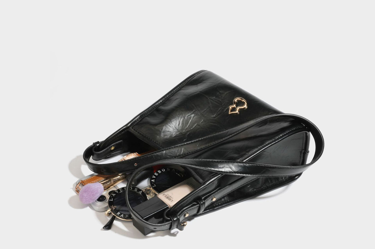 Strukturierte, trapezförmige Schultertasche aus glänzender, geknautscht wirkender Lederoptik mit goldfarbenen Beschlägen auf der Vorderseite und langem, verstellbarem