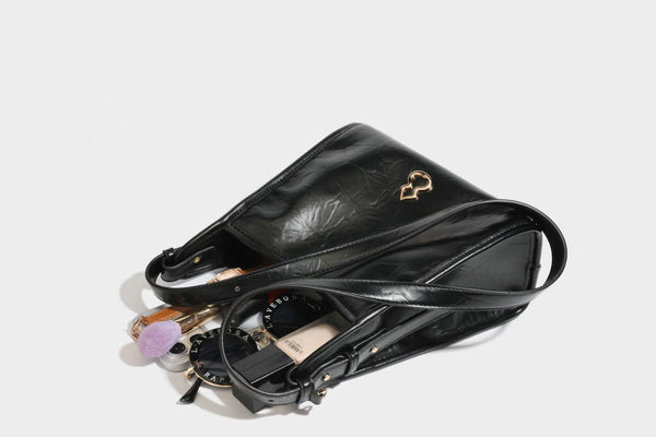 Strukturierte, trapezförmige Schultertasche aus glänzender, geknautscht wirkender Lederoptik mit goldfarbenen Beschlägen auf der Vorderseite und langem, verstellbarem