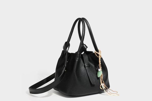Pebbled leather-look bucket tote bag with rolled double handles, drawstring closure, braided cord charm, and detachable