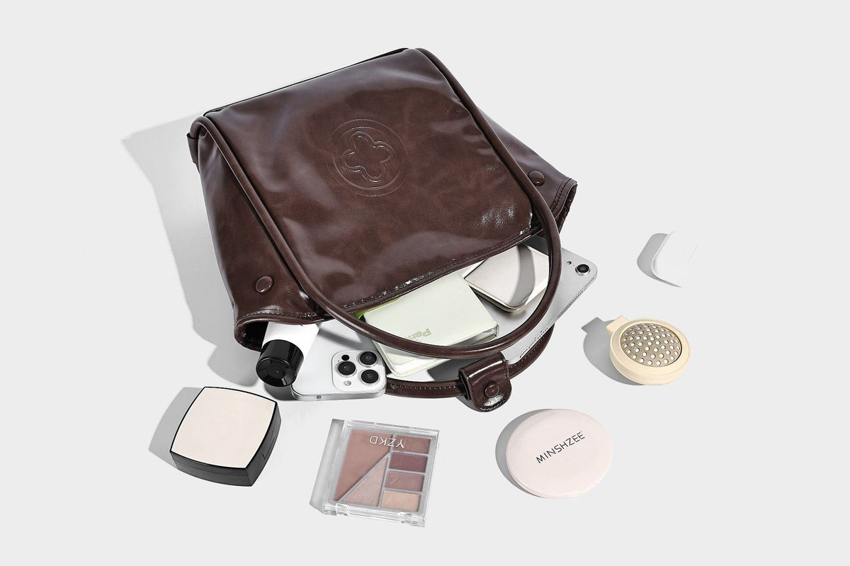 Glossy leather-look structured tote bag with rounded top handles, detachable shoulder strap, embossed front emblem, and side