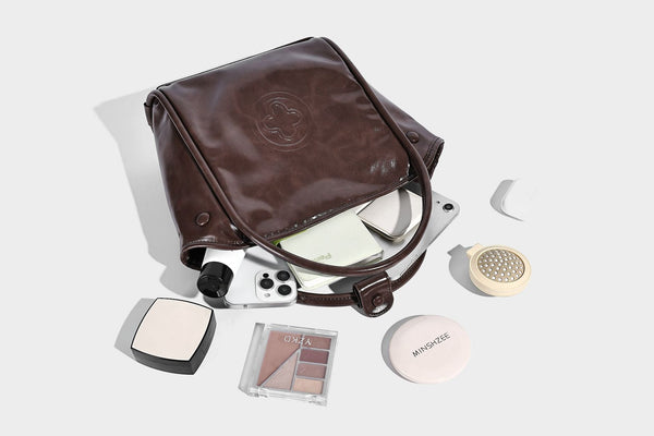 Glossy leather-look structured tote bag with rounded top handles, detachable shoulder strap, embossed front emblem, and side