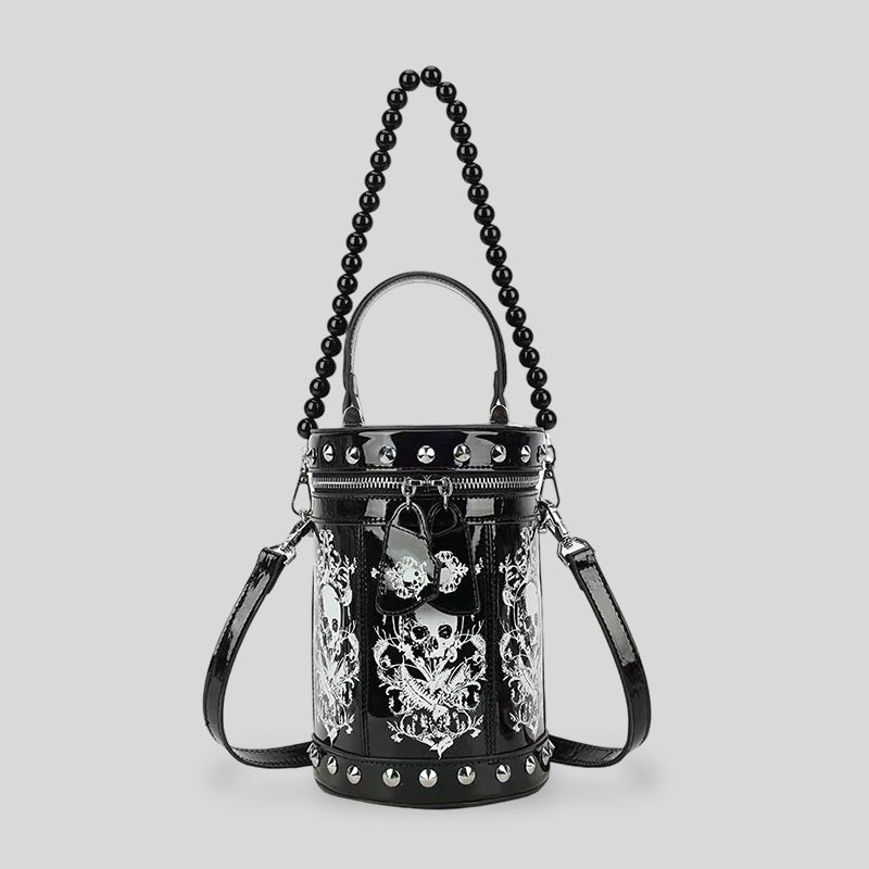 Black glossy cylindrical barrel bag with white skull-floral print panels, silver pyramid studs, black beaded top handle, and