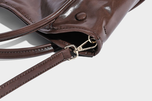 Glossy leather-look structured tote bag with rounded top handles, detachable shoulder strap, embossed front emblem, and side