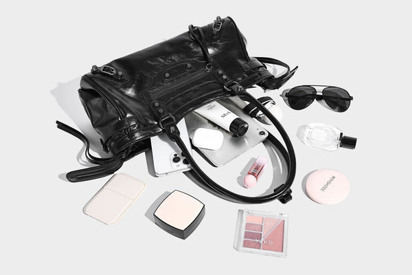 Längliche Schultertasche in Zylinderform mit glänzender Lederoptik, silberfarbenen Nietenbeschlägen, seitlichen Quasten und mehreren außenliegenden Reißverschlüssen