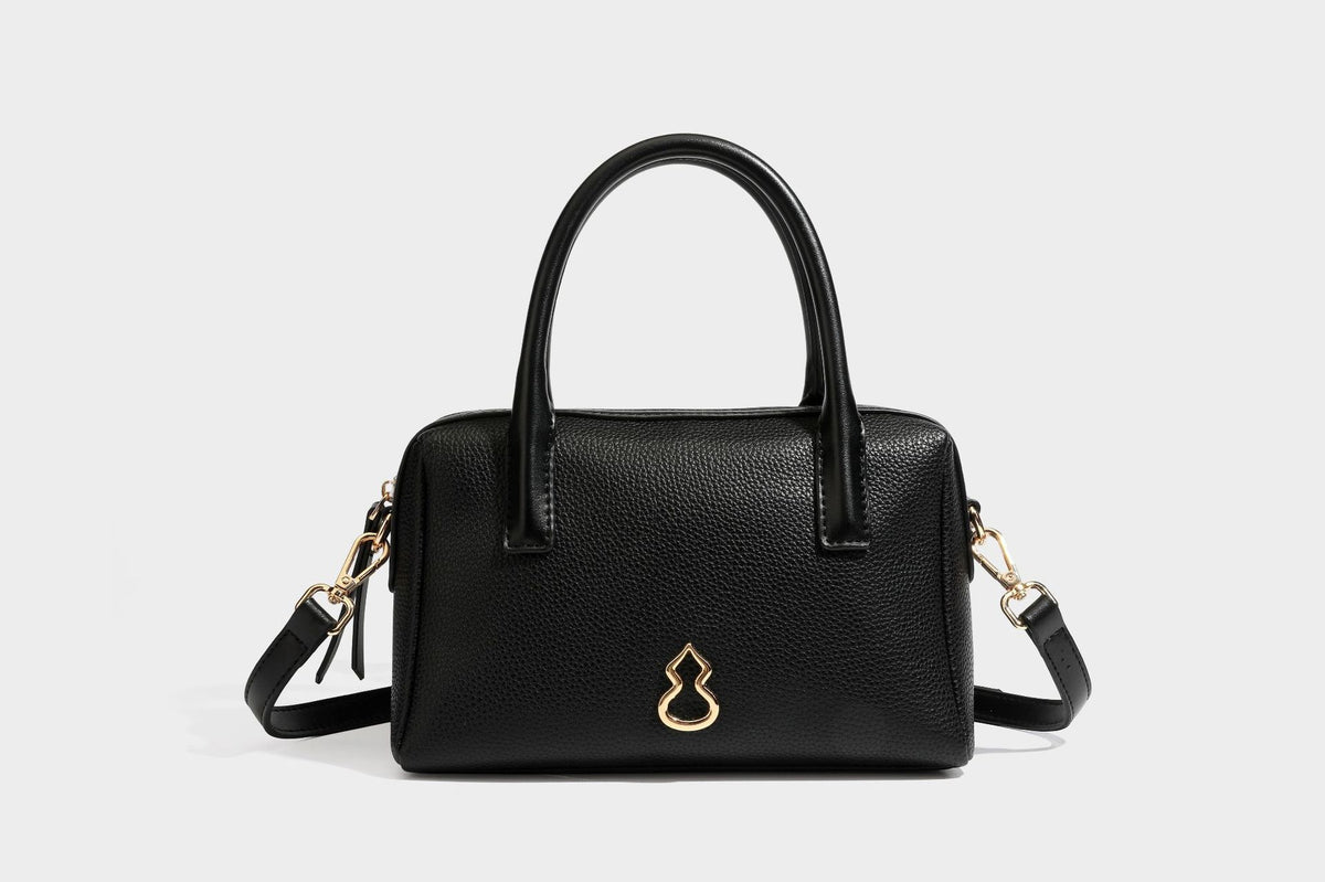 Small structured pillow satchel bag with pebbled leather-look finish, dual rolled top handles, gold-tone gourd emblem, and