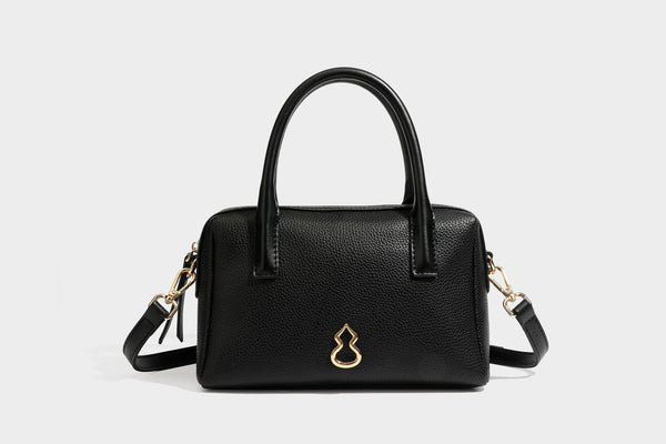 Small structured pillow satchel bag with pebbled leather-look finish, dual rolled top handles, gold-tone gourd emblem, and
