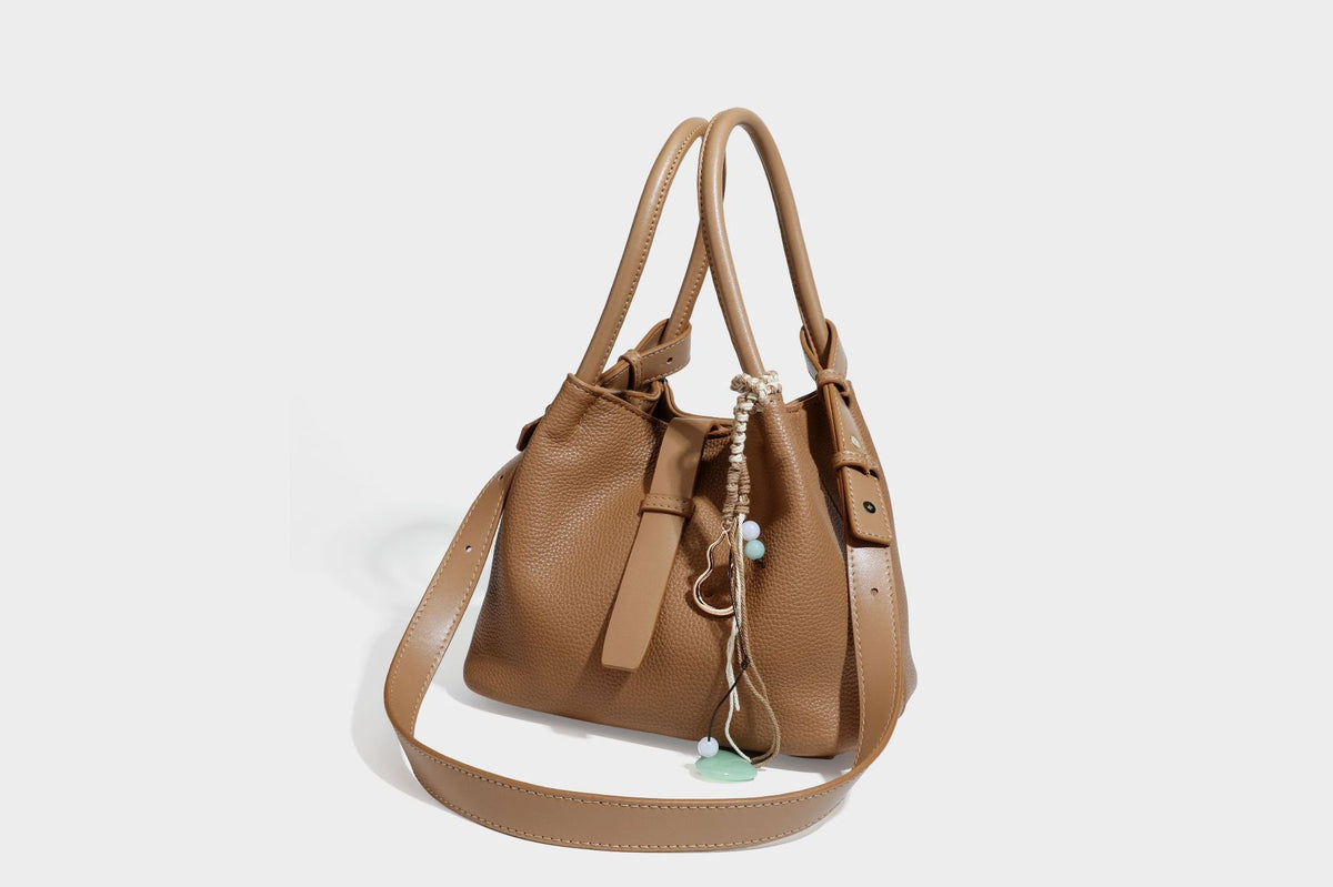 Pebbled leather-look bucket tote bag with rolled double handles, drawstring closure, braided cord charm, and detachable