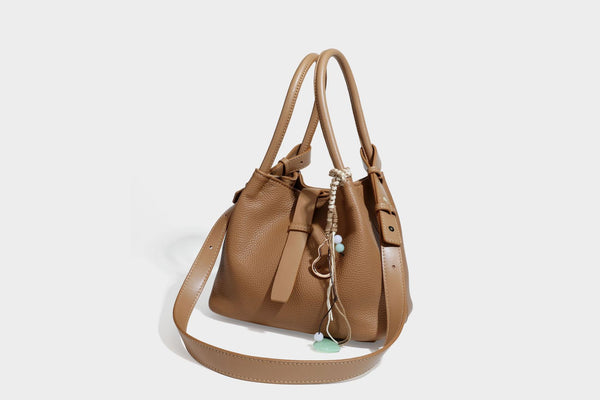 Pebbled leather-look bucket tote bag with rolled double handles, drawstring closure, braided cord charm, and detachable