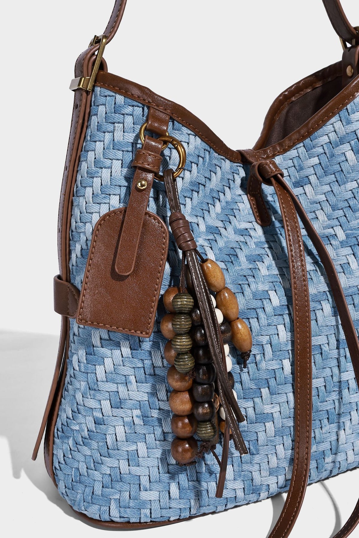 Light blue woven bucket bag with brown leather-look trim, gold-tone hardware, adjustable shoulder strap, and decorative bead