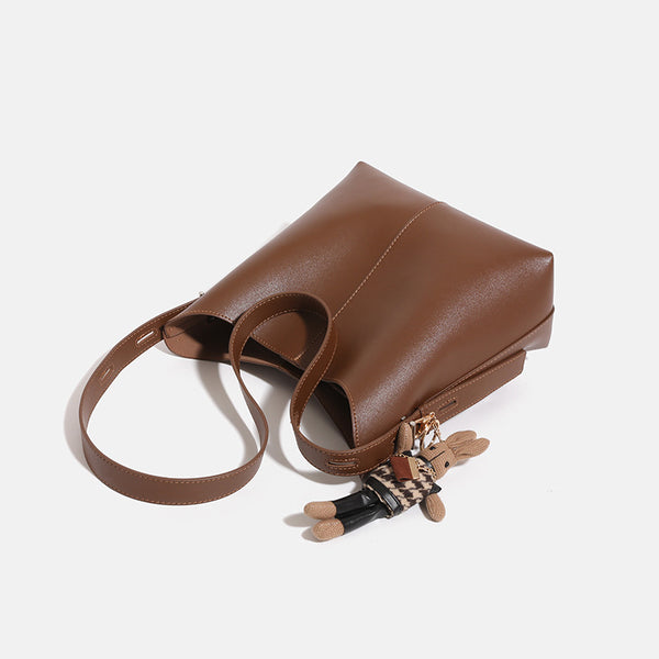 Smooth leather-look bucket bag with long flat shoulder strap, open top, gold-tone hardware, and decorative rabbit charm