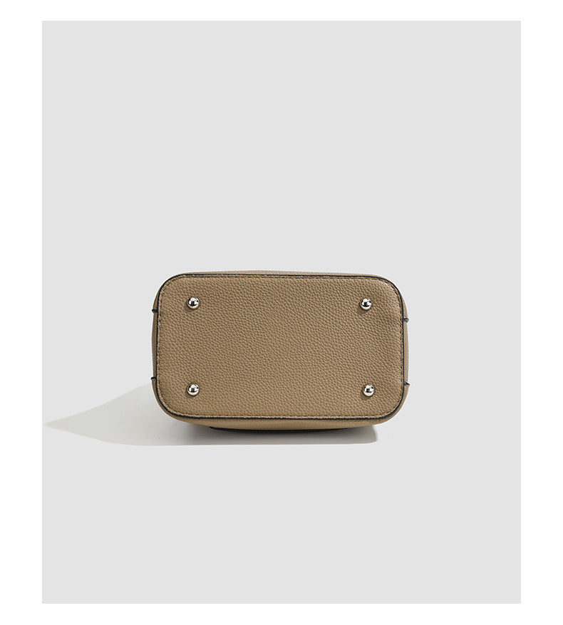 Structured taupe pebbled-texture bucket bag with top handle, silver ring hardware, tab-and-button closure, and knit bunny