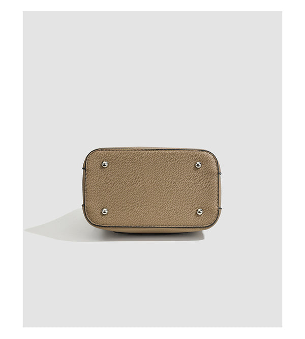 Structured taupe pebbled-texture bucket bag with top handle, silver ring hardware, tab-and-button closure, and knit bunny