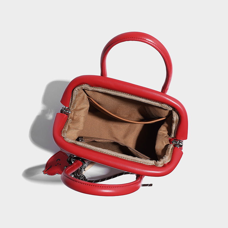 Small structured shell top-handle bag in red with heart charm and braided cord detail, smooth leather-look finish, detail