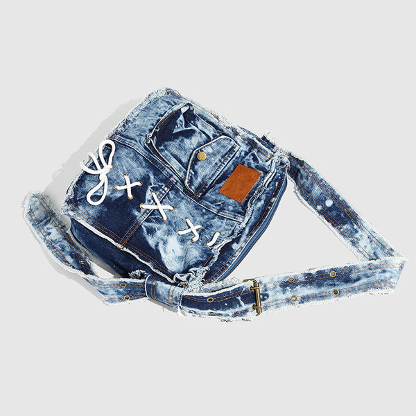 Slouchy distressed denim shoulder bag with frayed edges, white lace-up cross detail, front snap pocket, and long shoulder