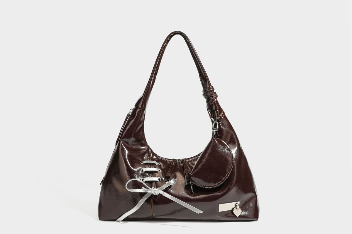 Weich fallende Hobo-Schultertasche in glänzender Lederoptik mit silberfarbenen Ösen zum Schnüren und Schleifenband auf der Vorderseite, Detailansicht