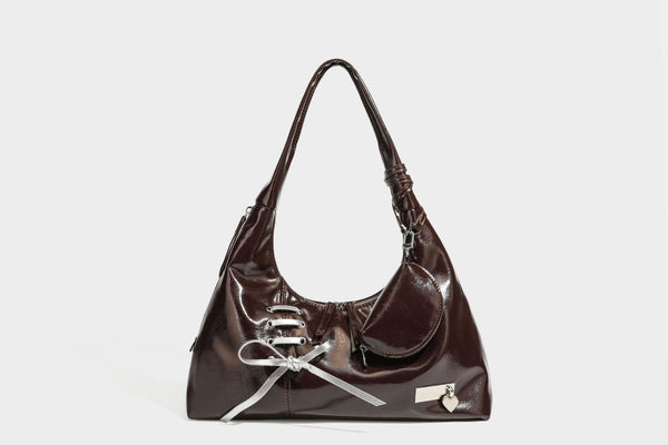 Weich fallende Hobo-Schultertasche in glänzender Lederoptik mit silberfarbenen Ösen zum Schnüren und Schleifenband auf der Vorderseite, Detailansicht