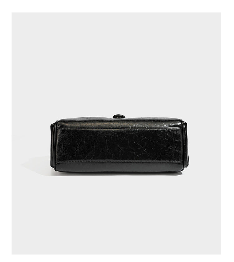 Glänzende, geknautschte Barrel-Satchel mit zwei oberen Tragegriffen, vorderem Klappen-Riemen-Panel, Ring- und Nietenbeschlägen sowie einem abnehmbaren