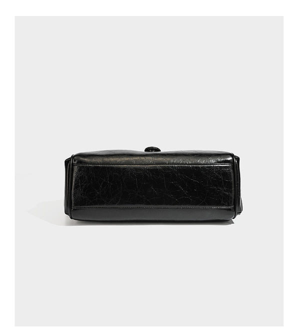 Glänzende, geknautschte Barrel-Satchel mit zwei oberen Tragegriffen, vorderem Klappen-Riemen-Panel, Ring- und Nietenbeschlägen sowie einem abnehmbaren