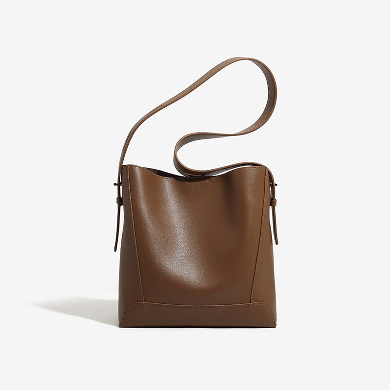 Structured smooth leather-look bucket shoulder bag with long adjustable strap and gold-tone buckle hardware in brown, detail