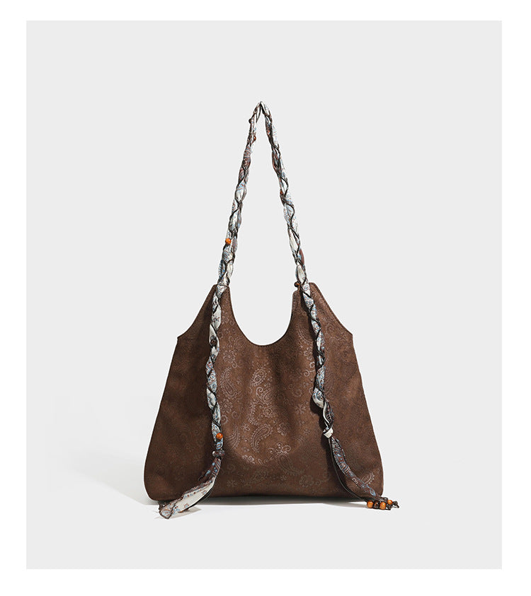 Slouchy paisley-embossed suede-look shoulder tote bag with braided patterned fabric straps and wood bead accents, detail view