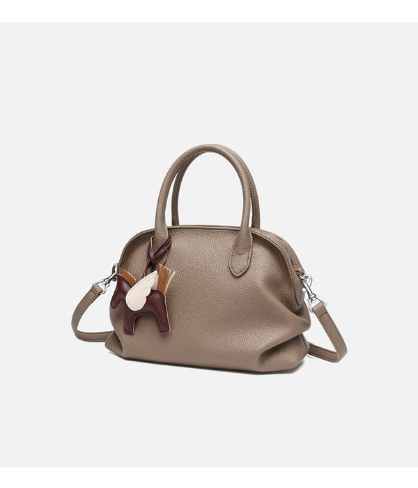 Rounded dome shell handbag in pebbled leather-look finish with twin top handles, zip closure, decorative horse charm, and
