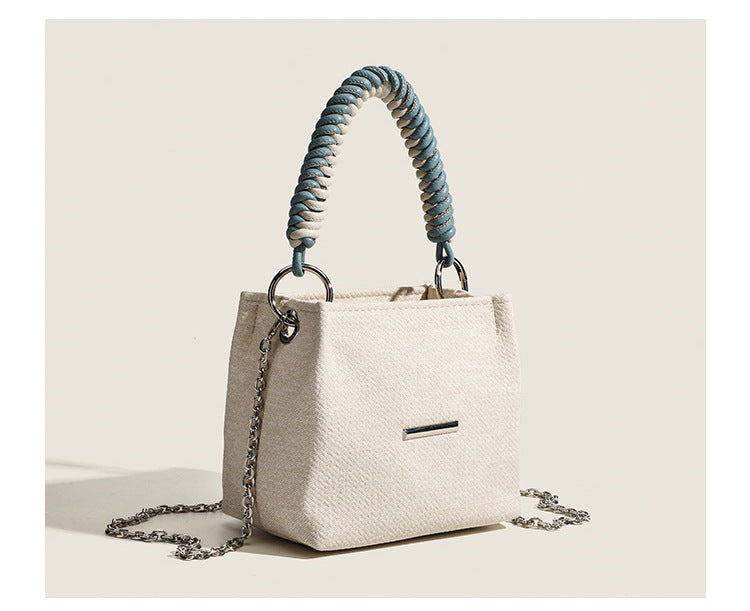 Small structured trapezoid mini bag with coiled rope top handle and silver-tone chain strap in textured fabric, detail view