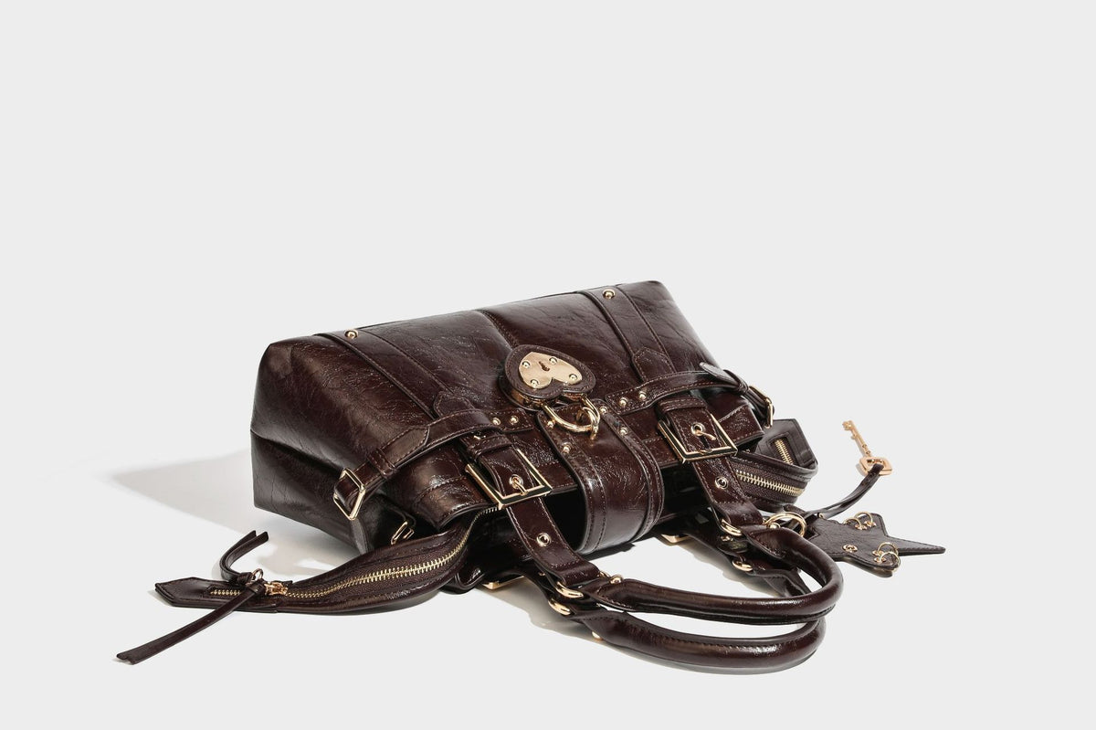 Structured leather-look satchel bag with heart padlock charm, star charm, gold-tone buckle hardware, dual top handles, and