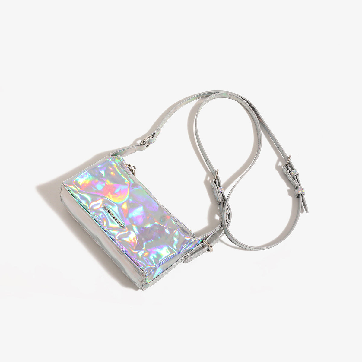 Kompakte rechteckige, holografisch schillernde silberfarbene Schultertasche mit Knitterstruktur, Reißverschluss oben und verstellbarem Schulterriemen