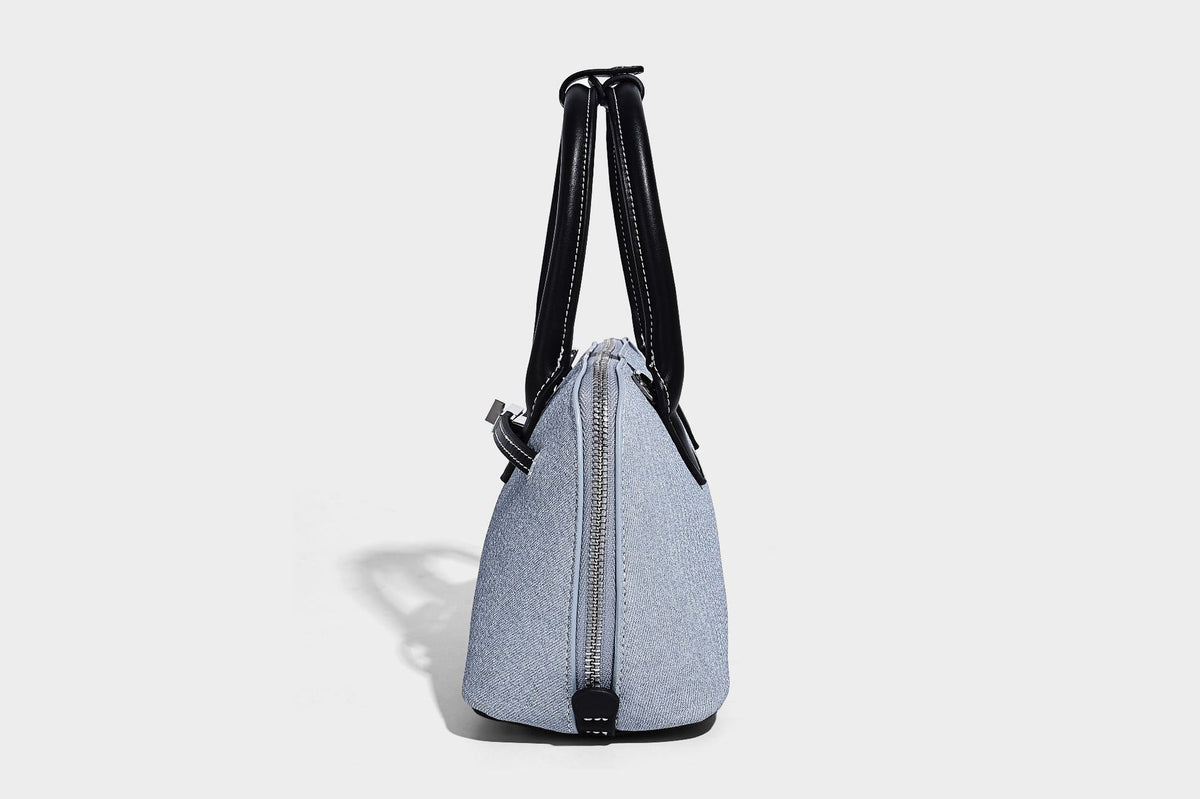 Compact structured satchel in light blue denim-look fabric with black leather-look trim, silver turn-lock closure, rolled