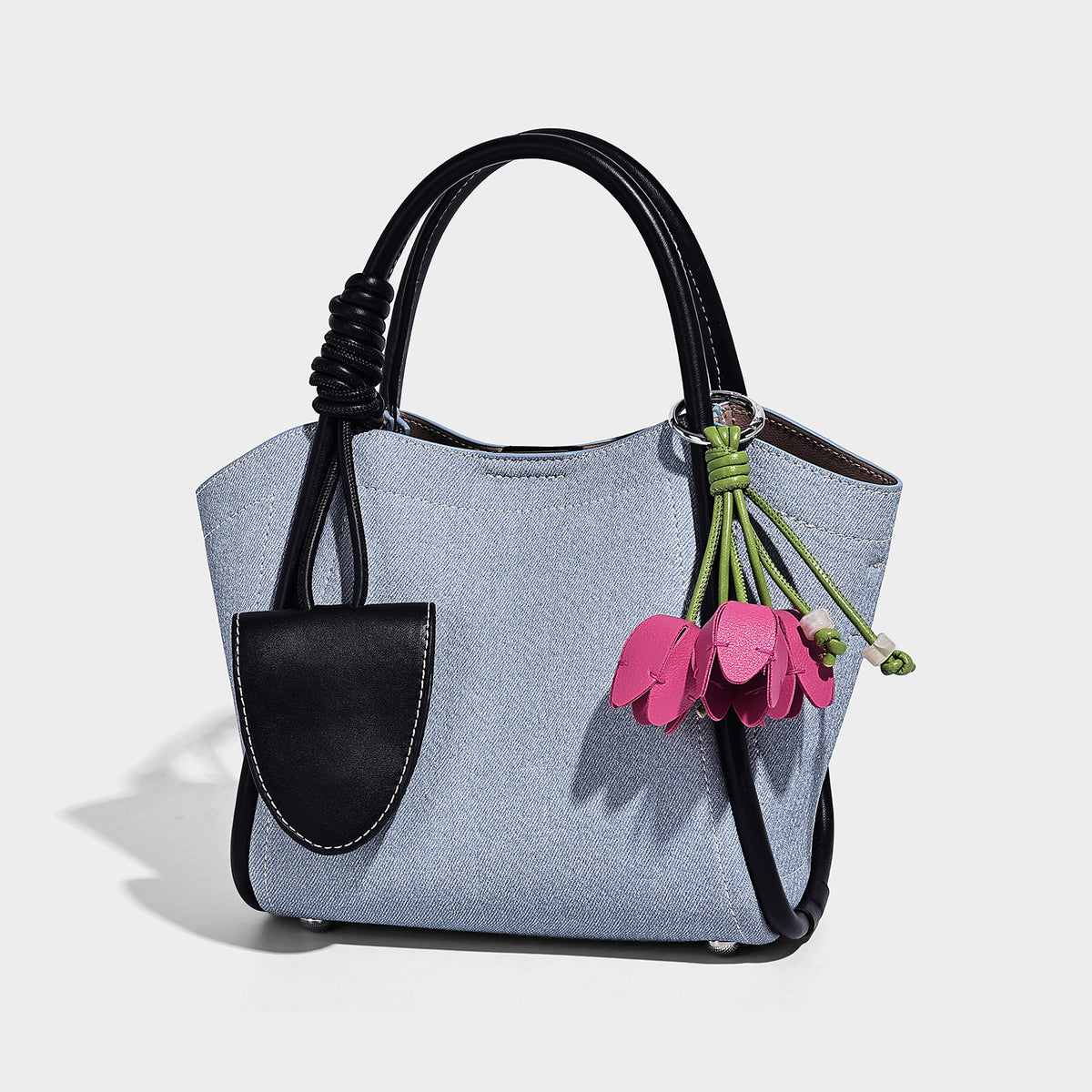 Light blue denim trapezoid tote bag with black leather-look trim, knotted top handles, detachable crossbody strap, front