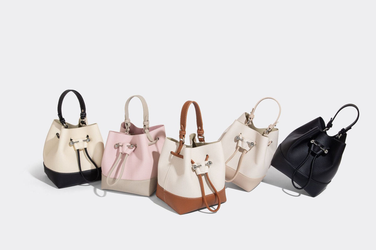 Small two-tone pebbled drawstring bucket bag with tan contrast base, metal toggle hardware, short top handle, and detachable