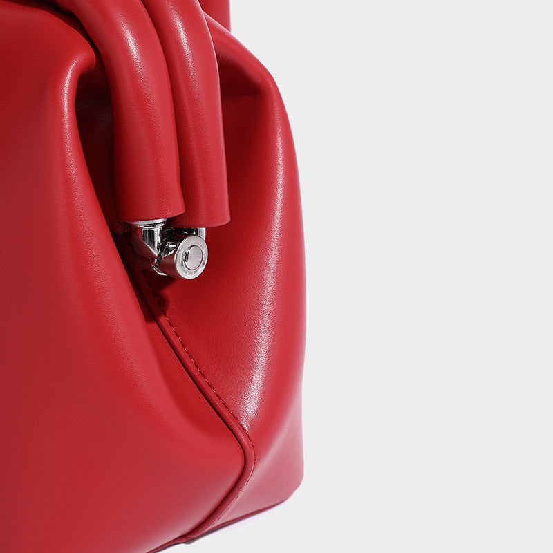 Small structured shell top-handle bag in red with heart charm and braided cord detail, smooth leather-look finish, detail