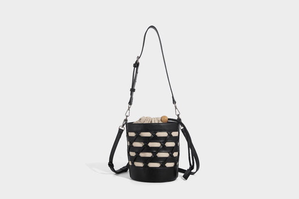 Small cylindrical woven lattice bucket bag with leather-look black trim, beige canvas body, wooden bead drawstring closure