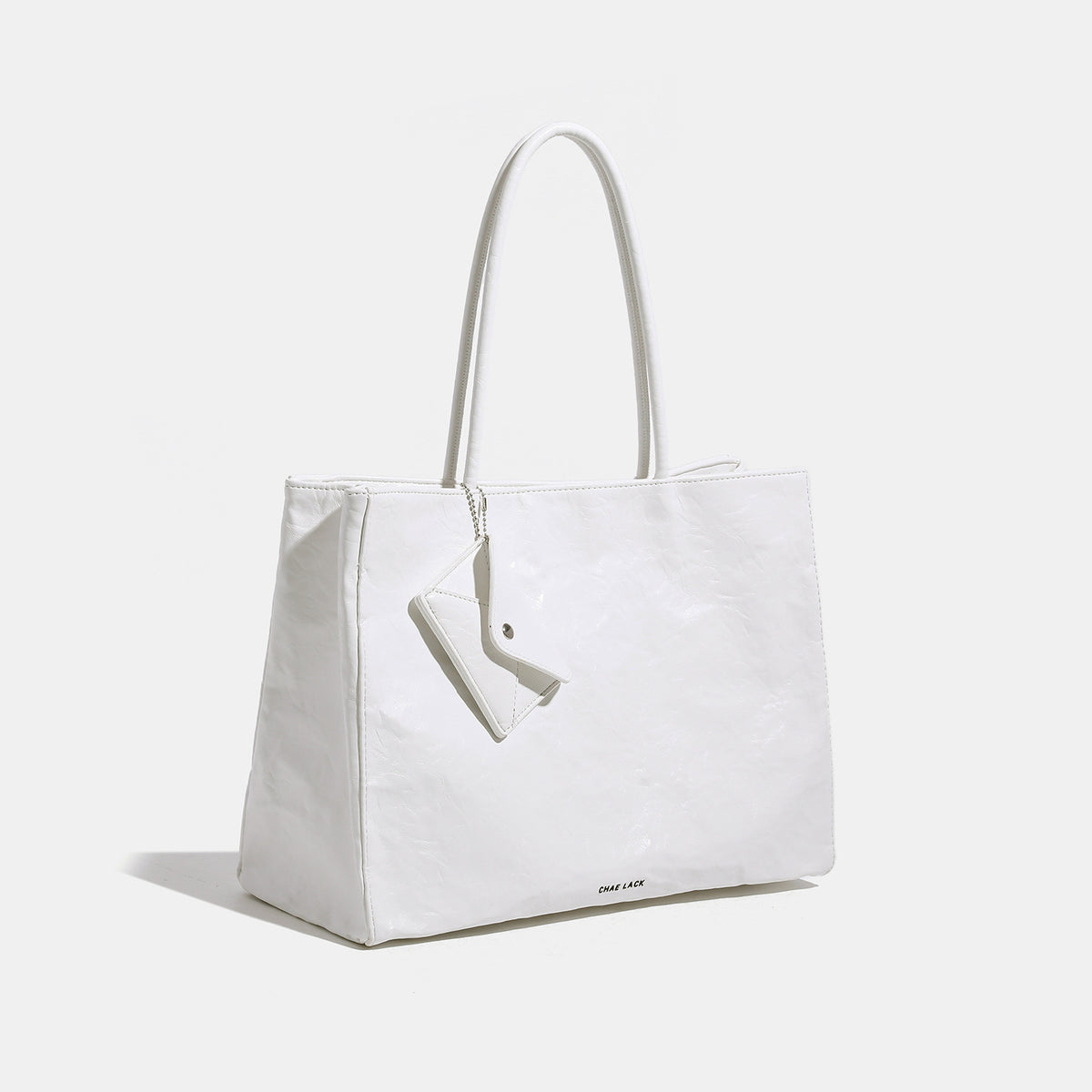 Structured rectangular crinkle leather-look tote bag with long rounded handles, zip top, and envelope-style hanging tag