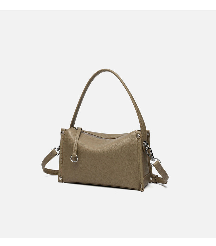 Small structured pebbled-finish convertible bag with silver corner studs, zip top, and detachable shoulder strap, detail view