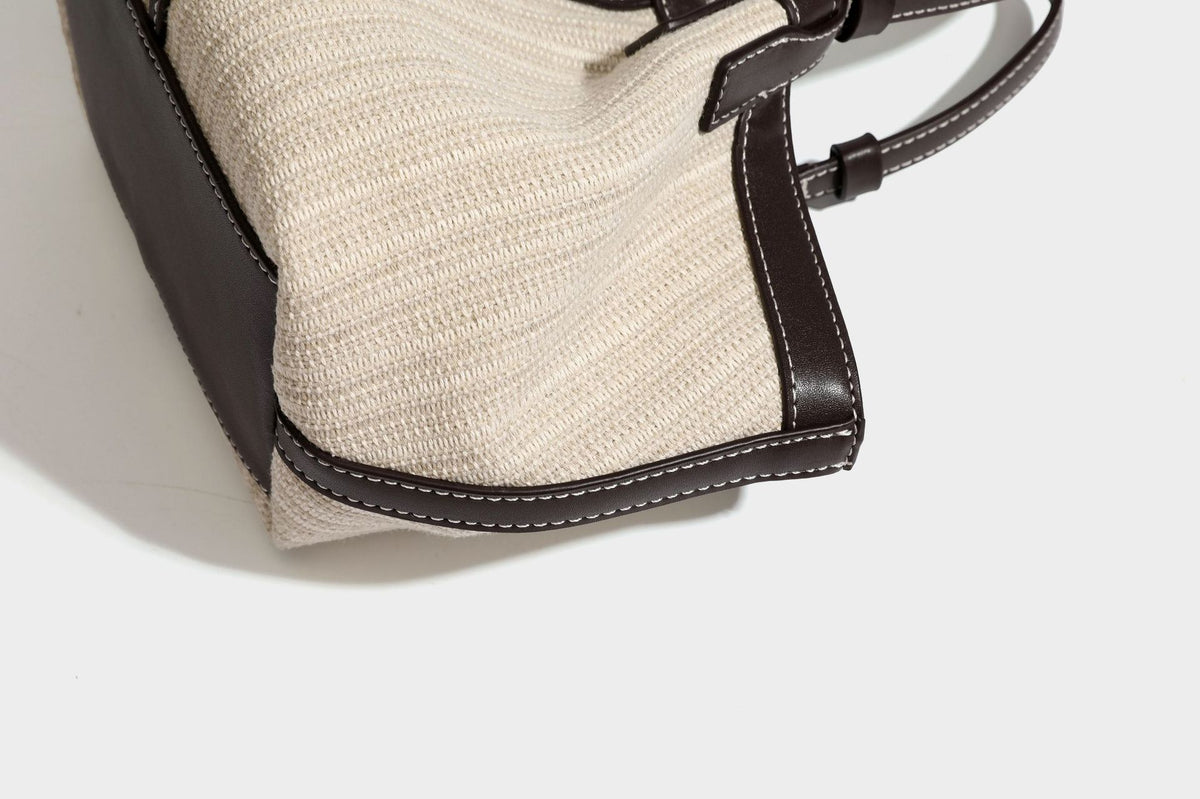 Cremefarbene geflochtene Tote-Bag mit dunkelbraunen Besätzen in Lederoptik, kontrastierenden weißen Nähten, zwei oberen Henkeln und abnehmbarem Schulter