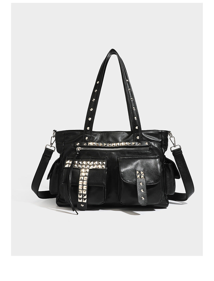 Black leather-look tote bag with silver pyramid studs on handles and front panel, multiple flap and zip exterior pockets