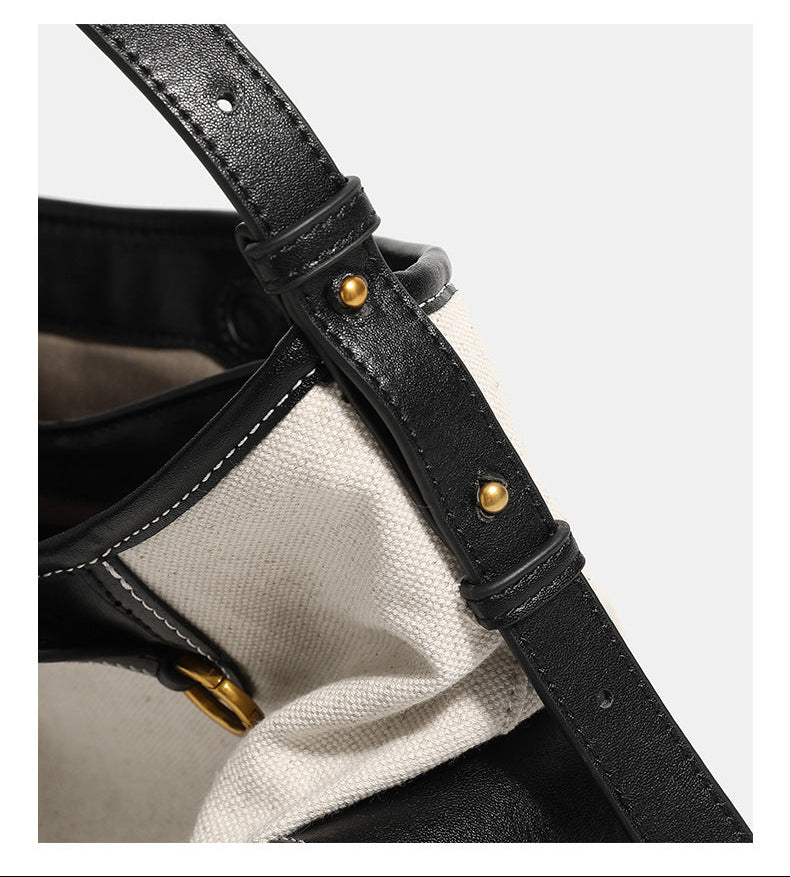 Off-white canvas shoulder bag with black leather-look trim, gold-tone ring hardware, top zip closure, side flap pocket, and
