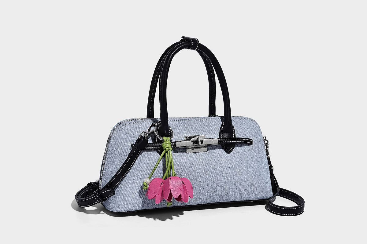Compact structured satchel in light blue denim-look fabric with black leather-look trim, silver turn-lock closure, rolled