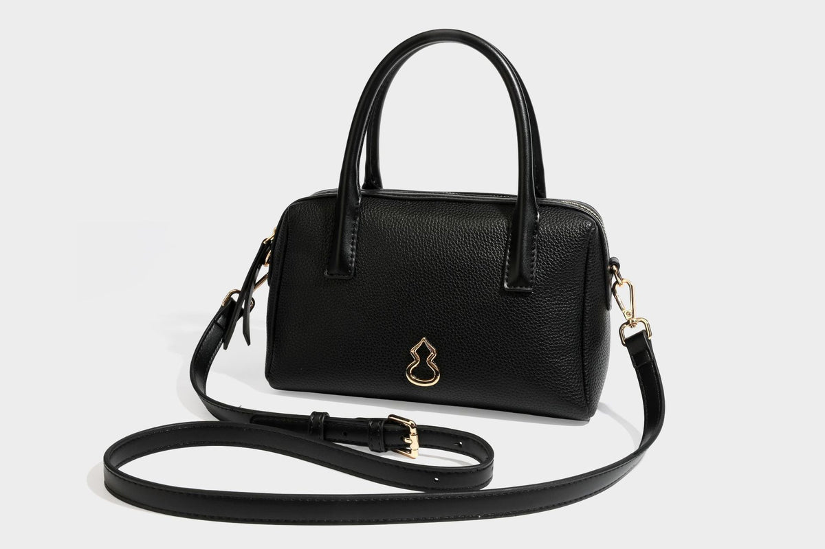 Small structured pillow satchel bag with pebbled leather-look finish, dual rolled top handles, gold-tone gourd emblem, and