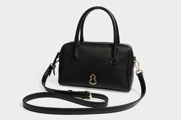 Small structured pillow satchel bag with pebbled leather-look finish, dual rolled top handles, gold-tone gourd emblem, and