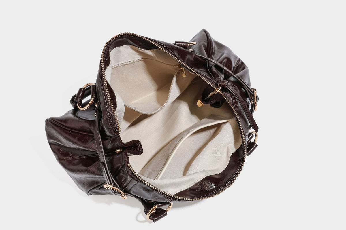 Glänzende Henkeltasche in Lederoptik mit zwei oberen Henkeln, goldfarbenen Nieten- und Ringbeschlägen, einem Riemendetail mit Schnalle auf der Vorderseite und